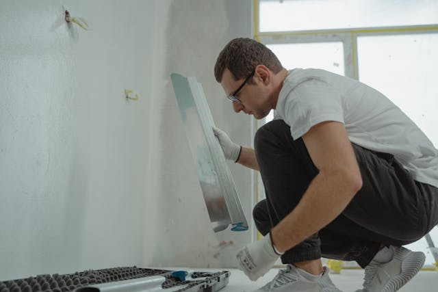 Person wearing safety glasses and gloves holding tools while crouched down